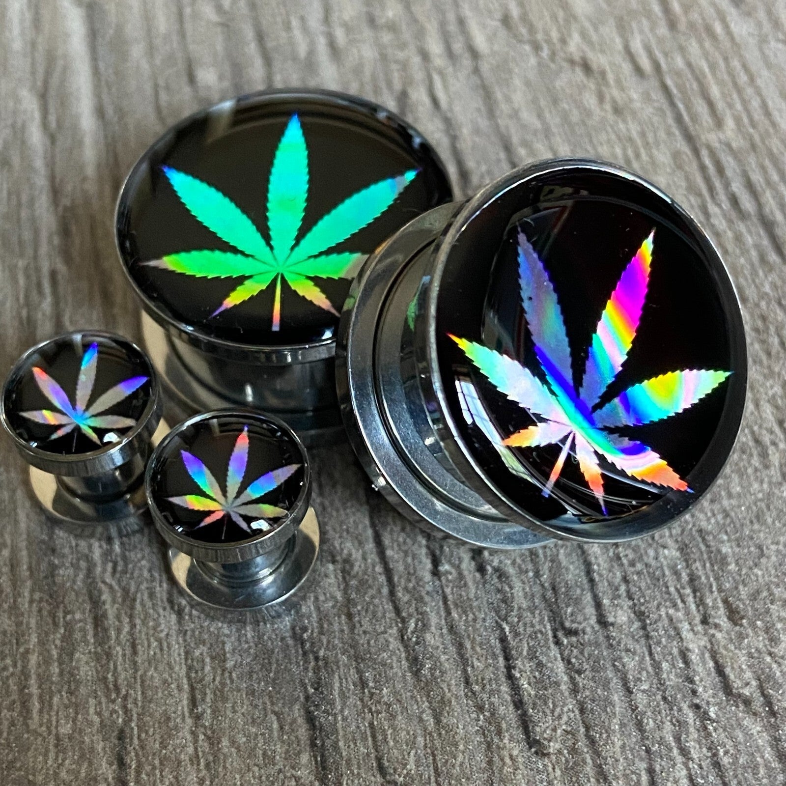 Pair of screw-on holographic pot leaf picture plugs in various sizes, made from stainless steel and resin.